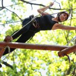 Young attractive woman climbing in adventure rope park in mountain helmet and safety equipment